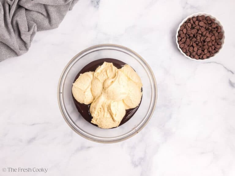 Half of the vanilla cake batter being stirred into melted chocolate in a glass bowl.