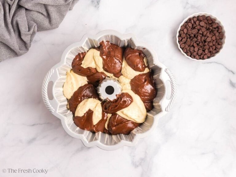 Marble cake batter dolloped into the bundt pan with a white bowl of chocolate chips.