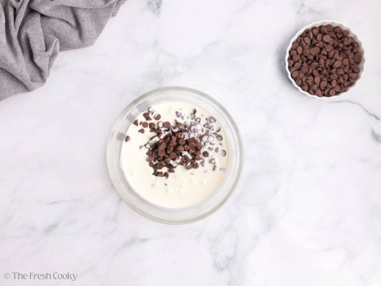 A white bowl of chocolate chips and cream with a second white bowl of chocolate chips.