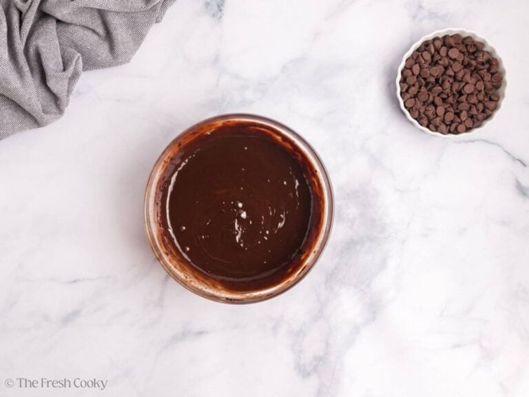 A glass bowl with chocolate ganache and a white bowl of chocolate chips.