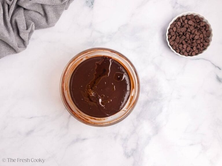 A glass bowl with chocolate glaze and a white bowl of chocolate chips to the right.