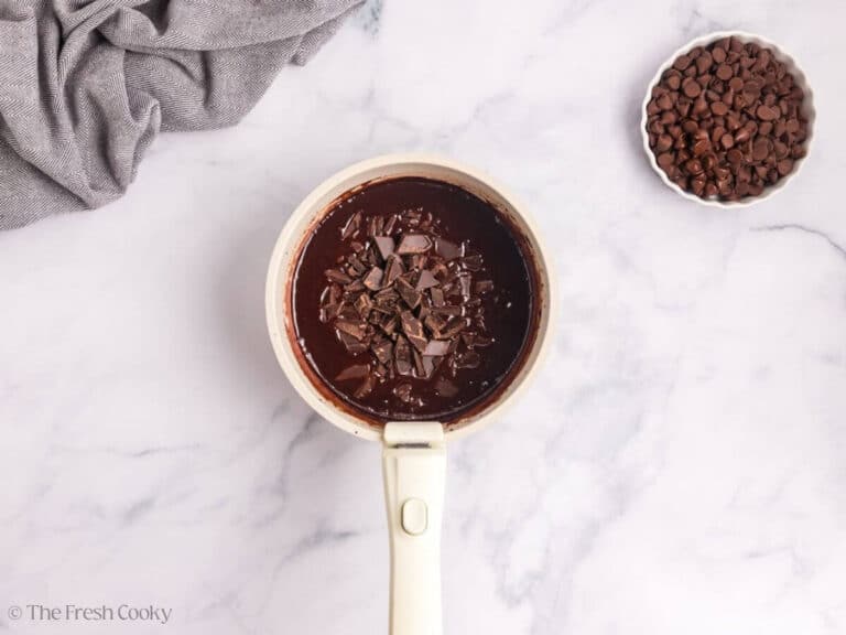 A saucepan with melted chocolate and more chopped chocolate added.