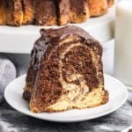 A slice of marble bundt cake on a white plate with the whole cake in the background.