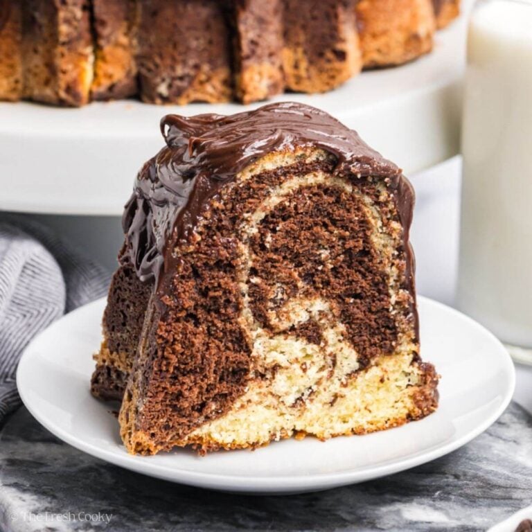 A slice of marble bundt cake on a white plate with the whole cake in the background.