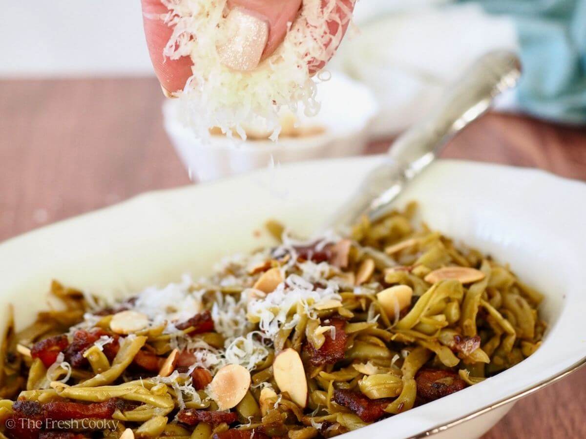 Hand adding additional grated parmesan cheese to southern green beans dish.
