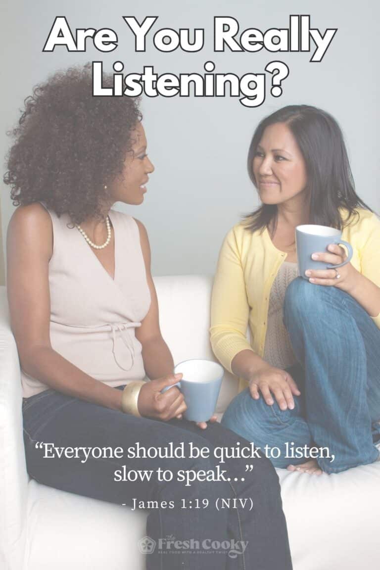 Two women sitting on a couch with a cup of coffee, one listening while the other is talking.