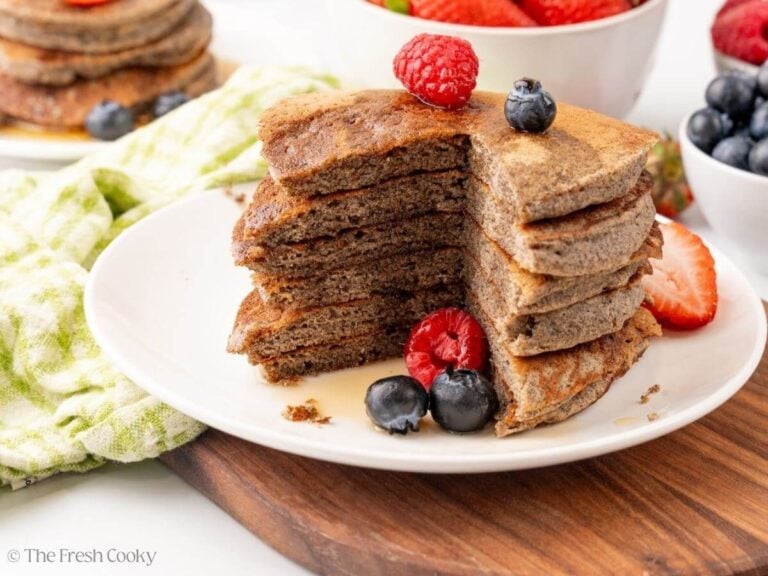 A stack of buckwheat pancakes on a white plate with berries.