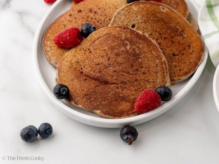 A white plate with buckwheat pancakes with berries.