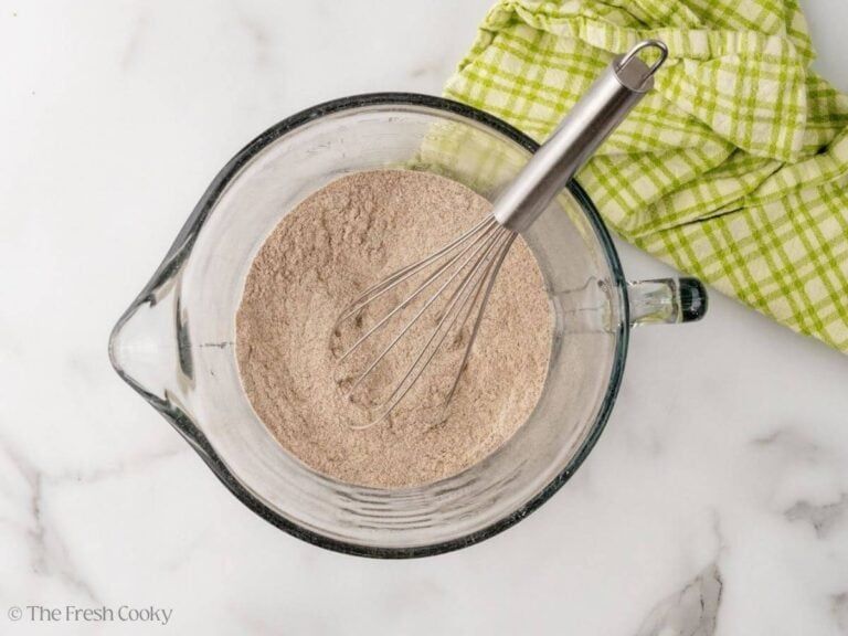 A large glass measuring cup with dry ingredients whisked together for buckwheat pancakes. A whisk is resting to the side.