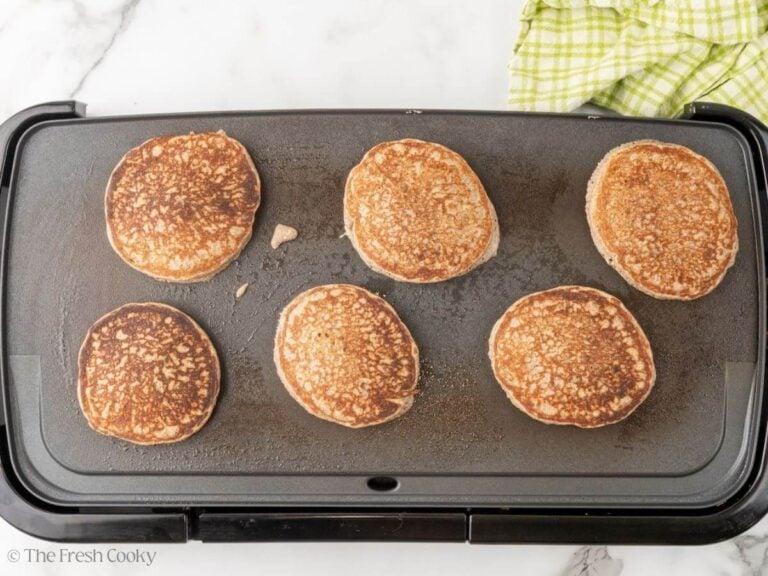 A griddle with buckwheat pancakes flipped and cooking on the second side.