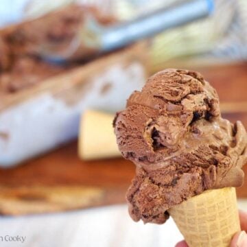 Chocolate Brownie ice cream scooped onto a sugar cone with the container of homemade ice cream in the background.