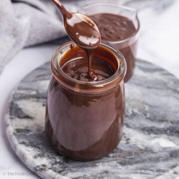 Spoon scooping up some chocolate ganache from a glass jar.