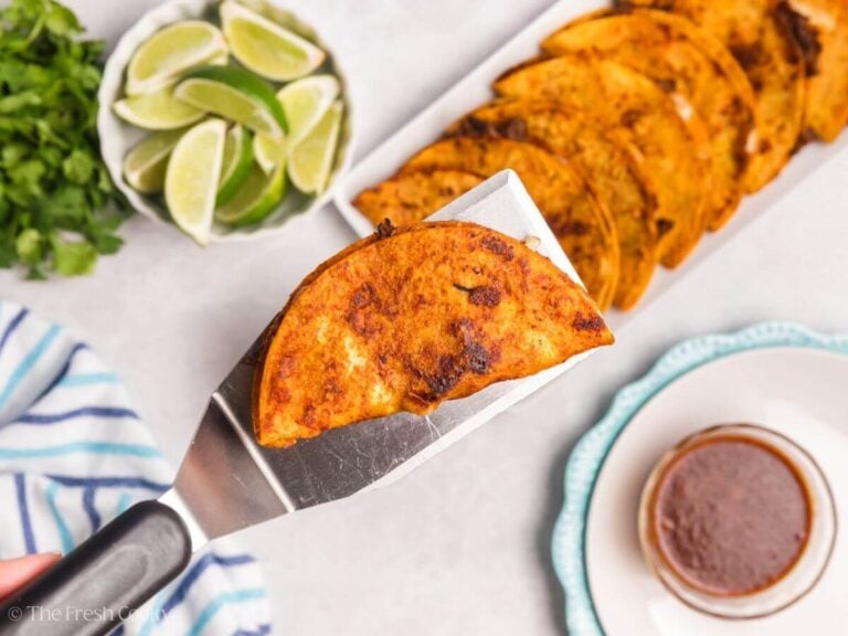 Birria taco on a meta spatula hovering over more tacos.