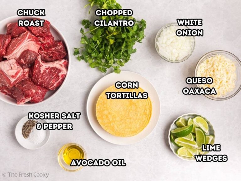 Labeled ingredients for birria tacos, L-R Chuck Roast, Cilantro, white onion, oaxaca cheese, limes, corn tortillas, avocado oil, salt and pepper.