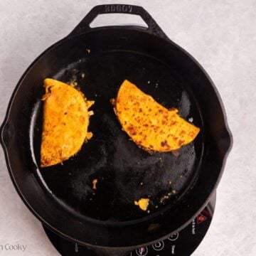 Birria tacos searing in a skillet.