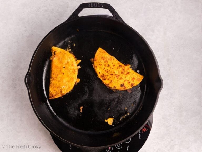 Birria tacos searing in a skillet.
