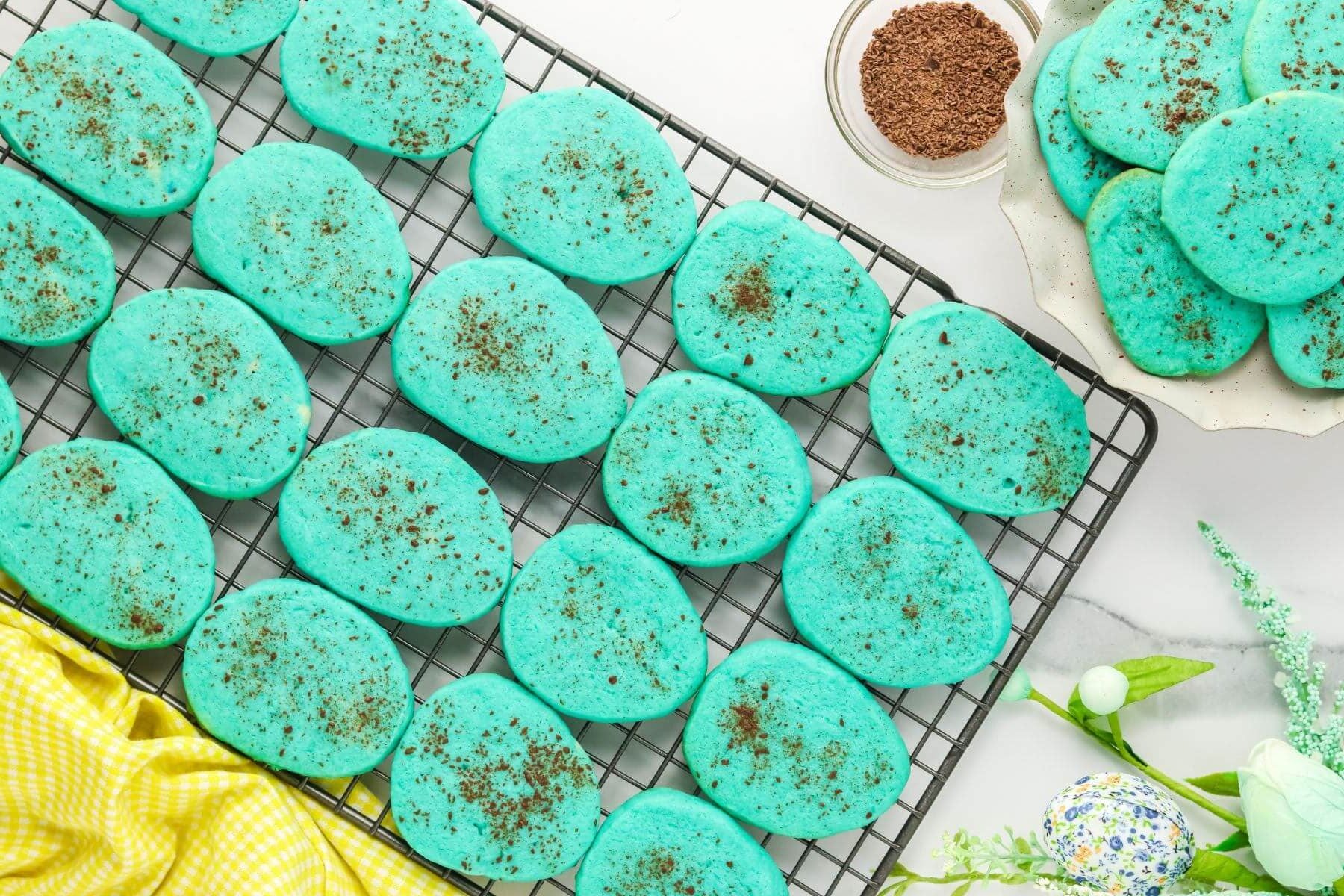 A pile of cookies sits next to a full cooling rack of more cookies.