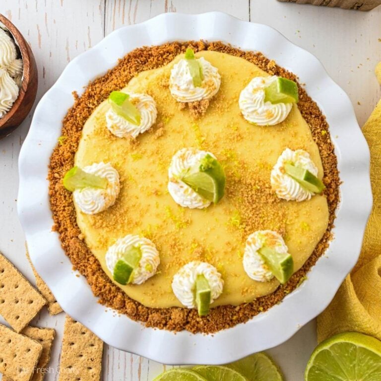 A key lime pie with swirls of whipped cream and garnished with key lime pieces.