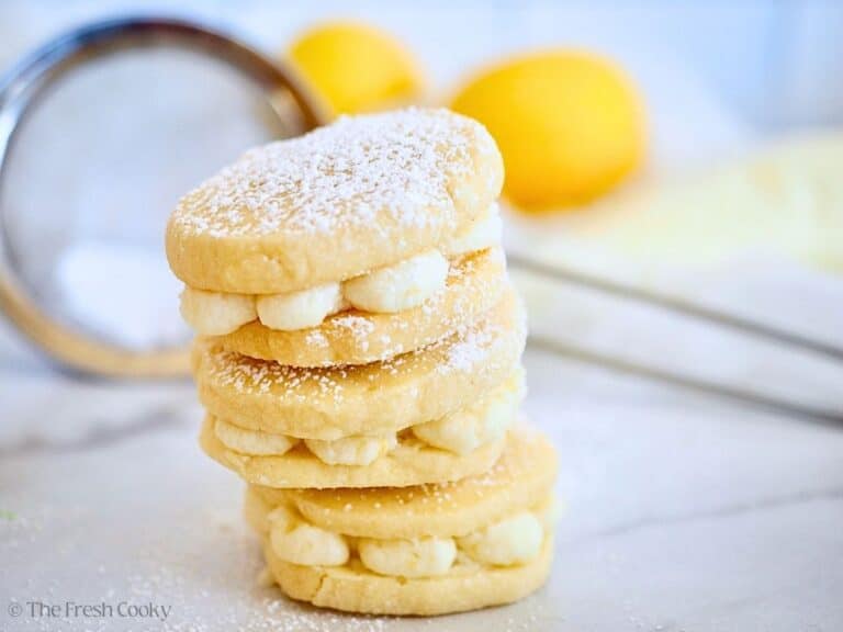 Stack of three lemon sandwich cookies on a marble counter, with lemons in background.