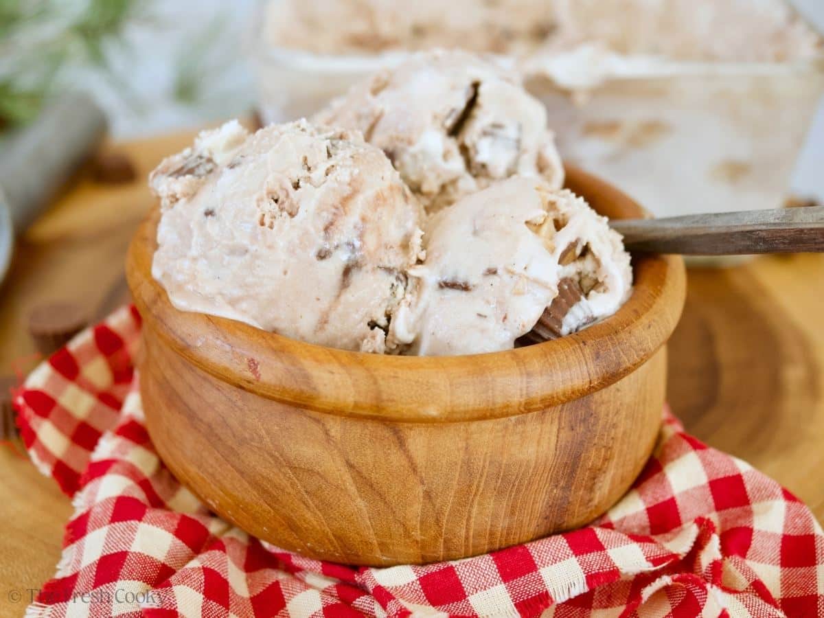 Three scoops of moose tracks ice cream in a wooden bowl with a spoon and gingham napkin.