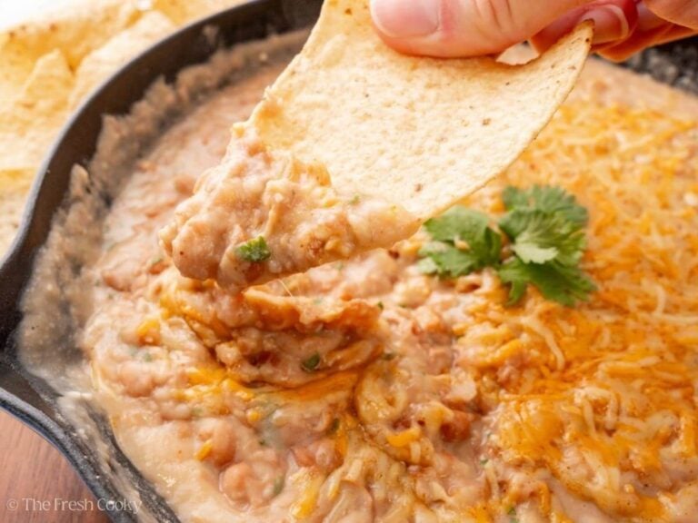 Hand dipping a chip into cheesy refried beans.