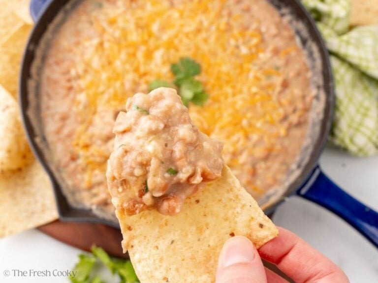 Overhead shot of a hand holding a tortilla chip with refried pinto beans on it.