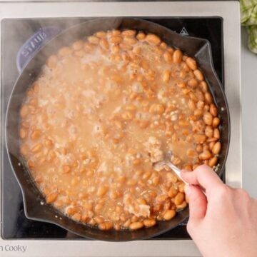 Fork smashing some beans while they are simmering in a skillet.