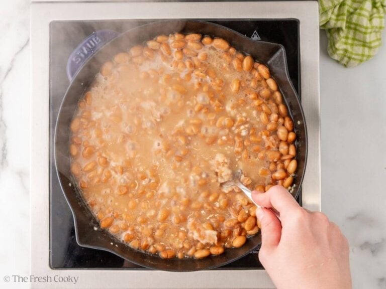 Fork smashing some beans while they are simmering in a skillet.