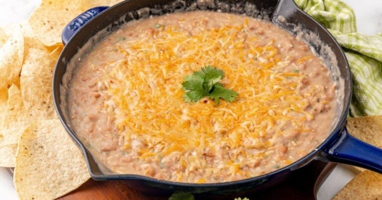 A cast iron pan filled with refried beans topped with melty cheese and some cilantro.