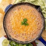 Refried pinto beans in a skillet with cheese on top served with chips on the side.
