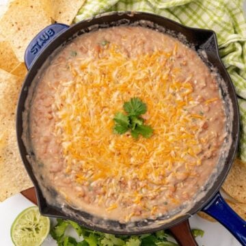 Refried pinto beans in a skillet with cheese on top served with chips on the side.