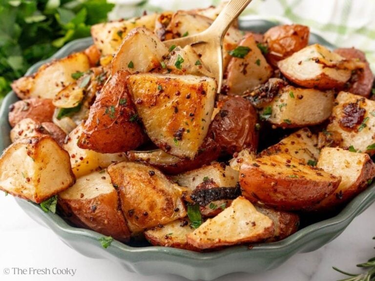 A green bowl with a gold spoon scooping up roasted potatoes with onions.