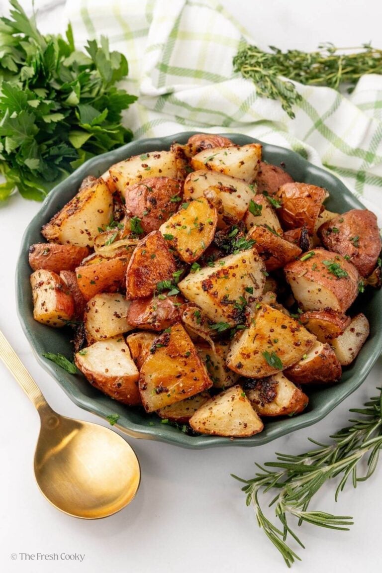 Roasted potatoes and onions in a green bowl with a gold spoon in front.