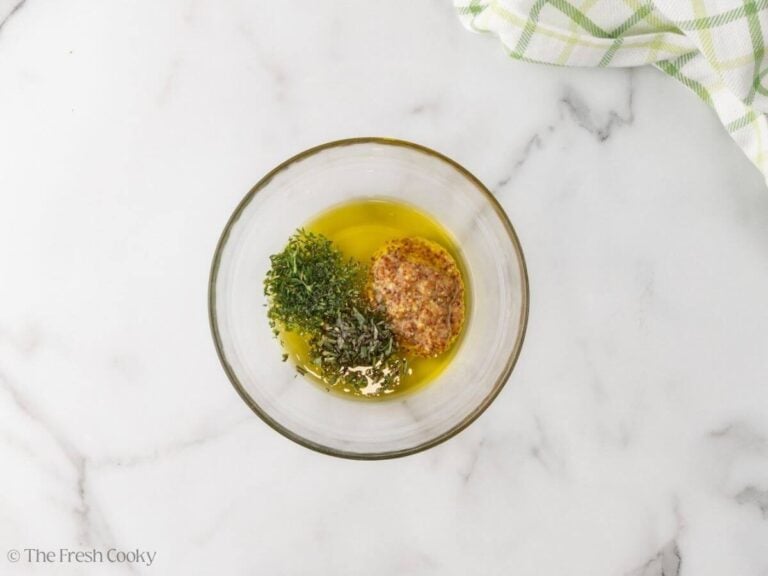 A glass bowl with olive oil, thyme, rosemary, and whole grain mustard.