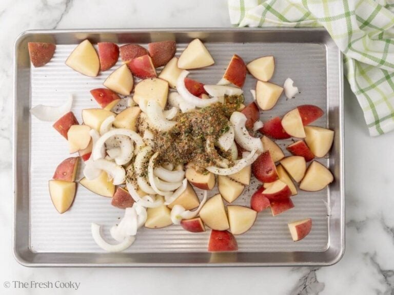 A sheet pan with potatoes, onions, and olive oil mustard mixture.