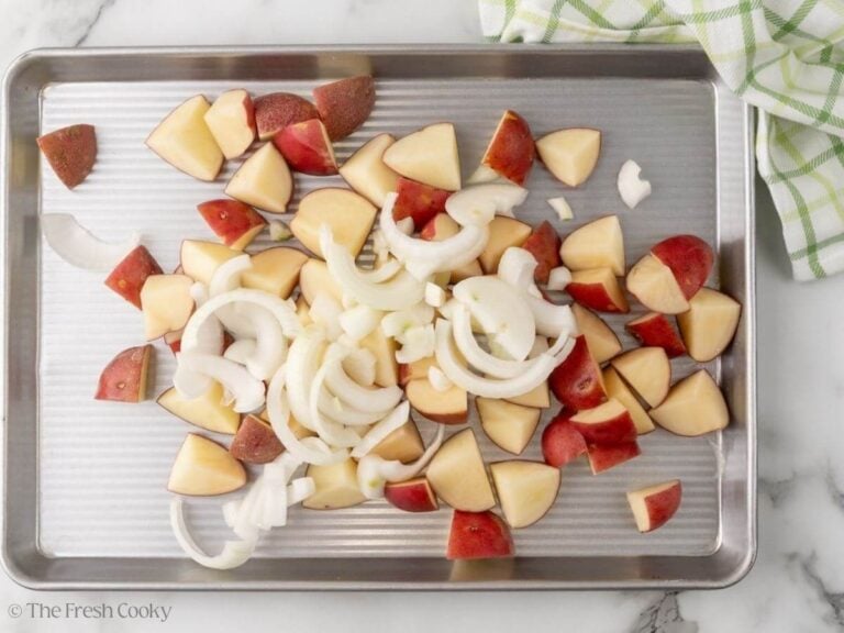 A sheet pan with a pile of red potatoes and onions.