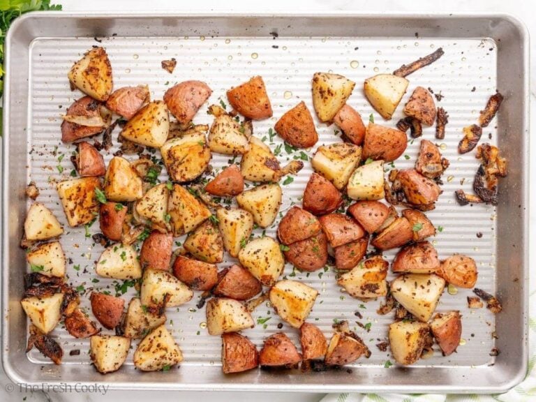A sheet pan with roasted potatoes with onions and chopped parsley on top.