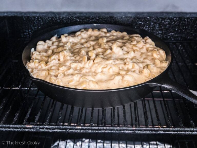 A cast iron pan filled with smoked mac and cheese, on a rack in smoker.