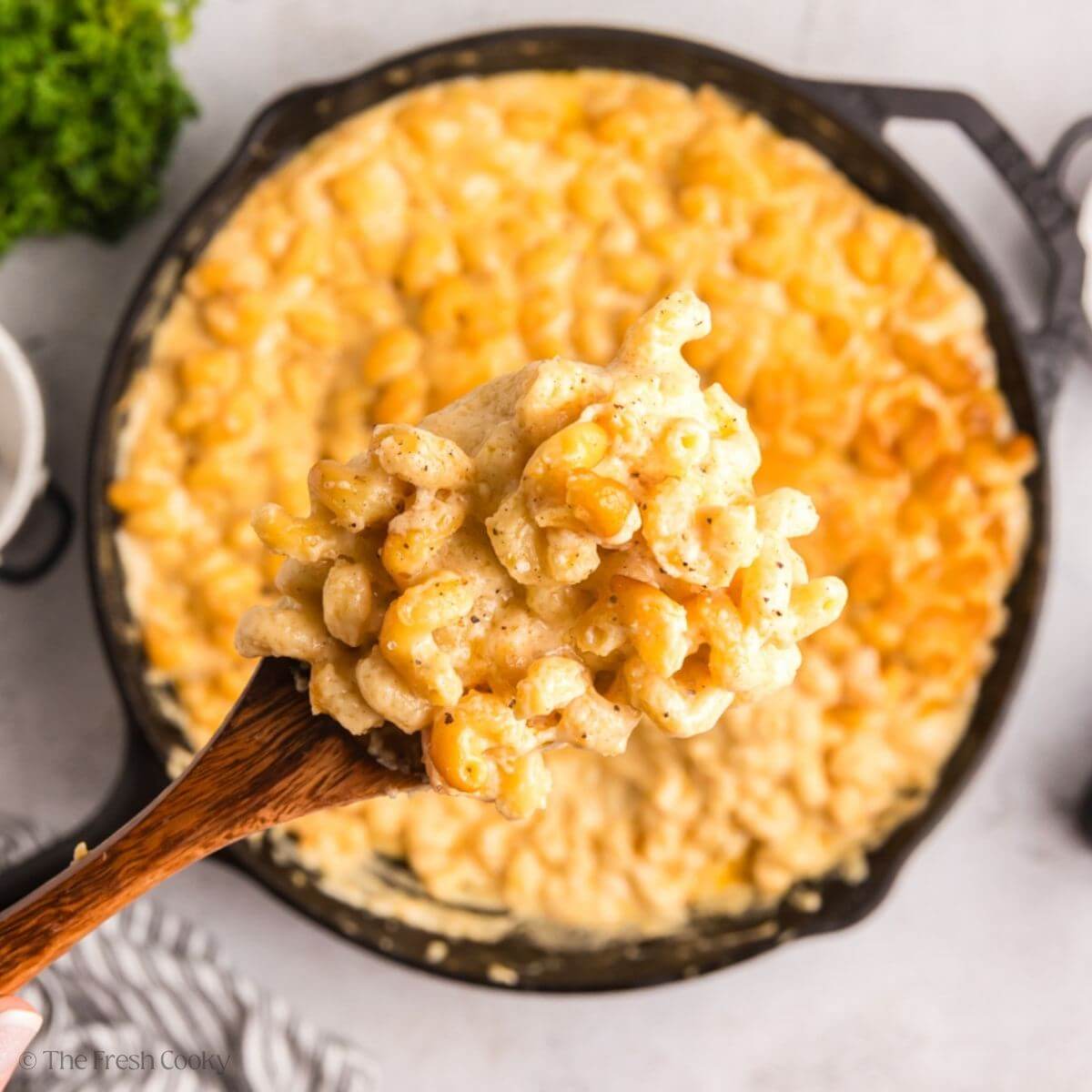 Smoked mac and cheese in a large cast iron skillet, with a wooden spoon holding a serving.