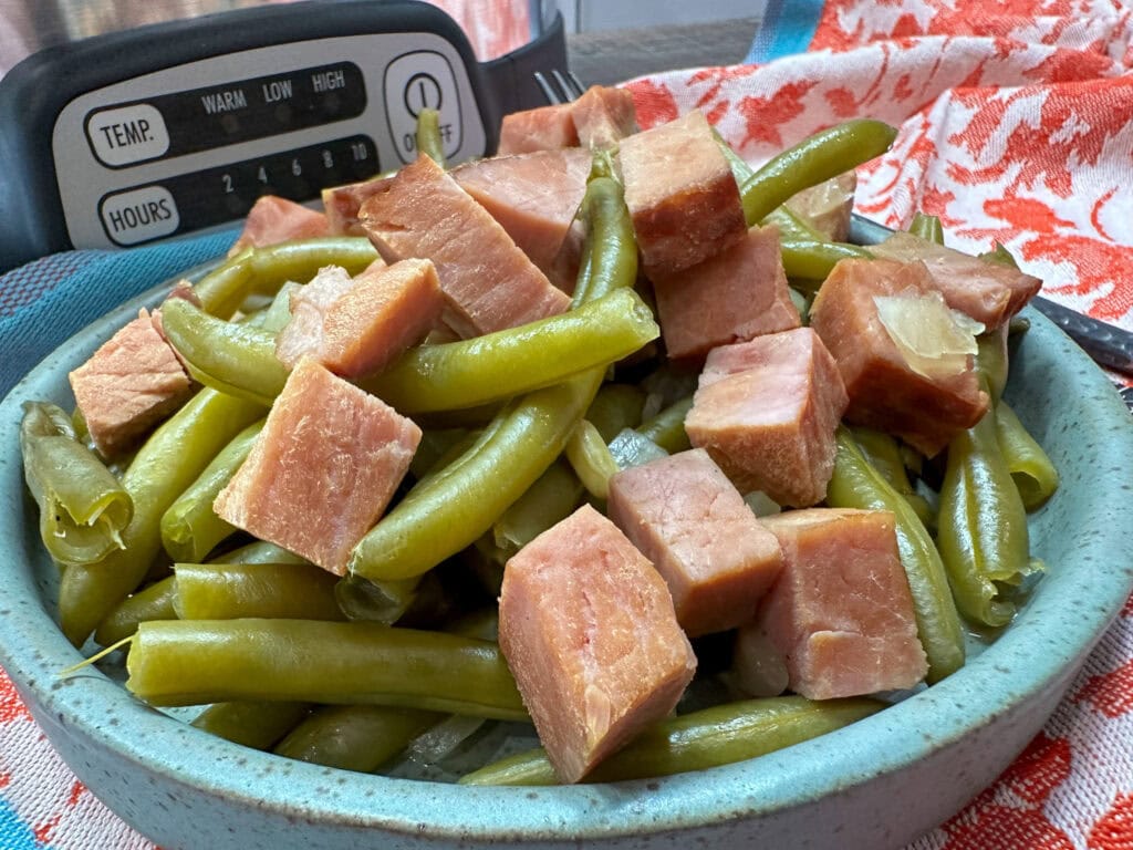 Green beans and ham chunks on a plate in front of a slow cooker.
