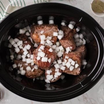 Barbacoa beef seared in crockpot with sauce and chopped onions.