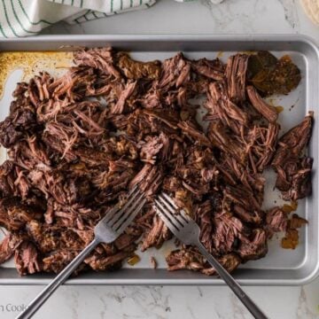 Two forks shredded the beef on a cookie sheet.