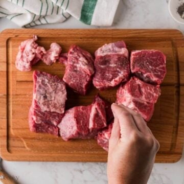 Hand sprinkling salt and pepper on beef chunks.