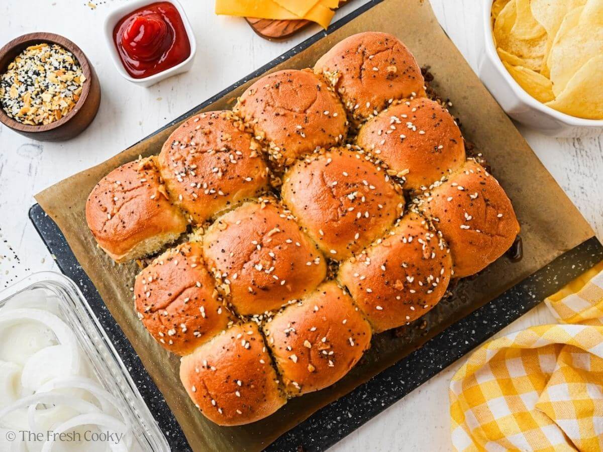 Top down looking at crispy buns sprinkled with everything bagel seasoning and condiments for cheeseburger sliders.