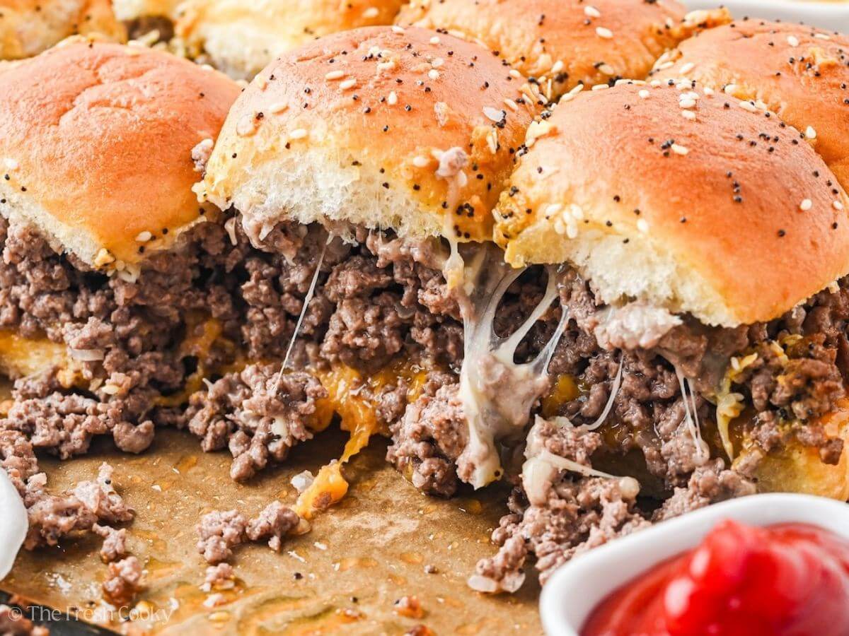 Side view of cheeseburger sliders in baking dish with ketchup nearby.