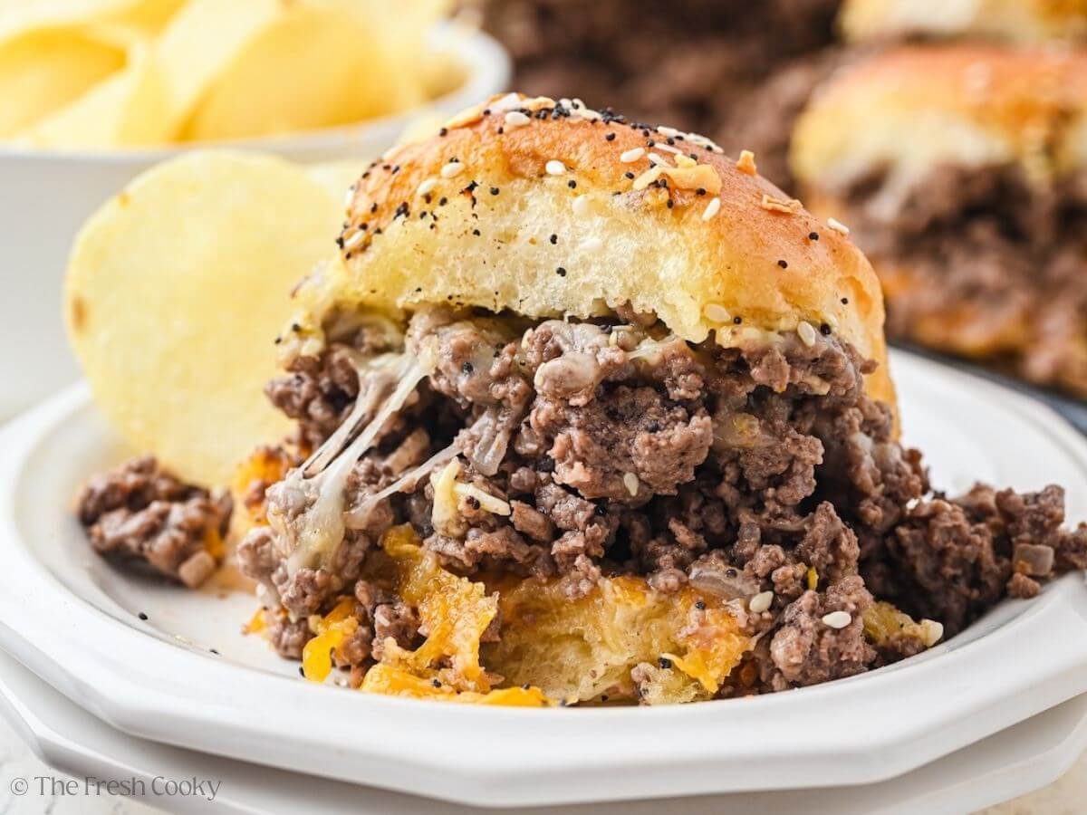 Cheeseburger slider on a plate with gooey cheese and potato chips.