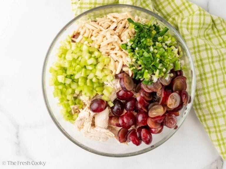 Celery, red grapes, shredded chicken, slivered almonds and green onions in glass bowl.
