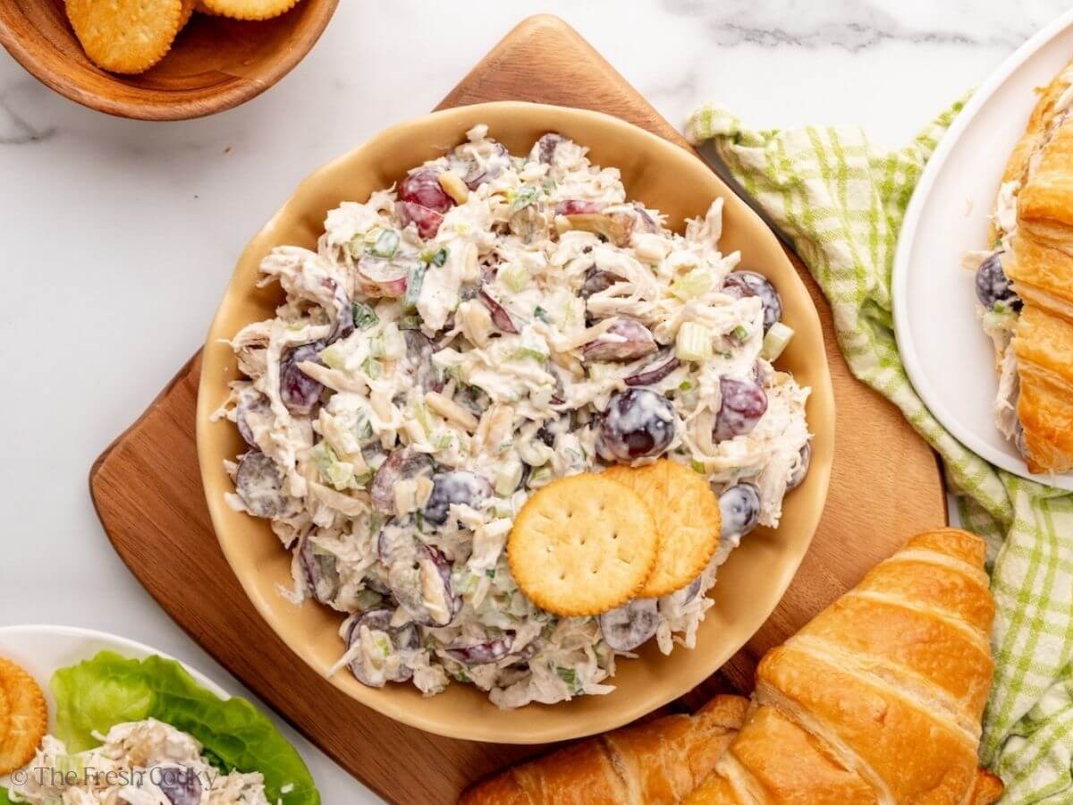 Chicken salad in a bowl with crackers and croissants nearby.