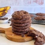 Stacked chocolate banana cookies one with a bite taken out of it revealing gooey chocolate inside.