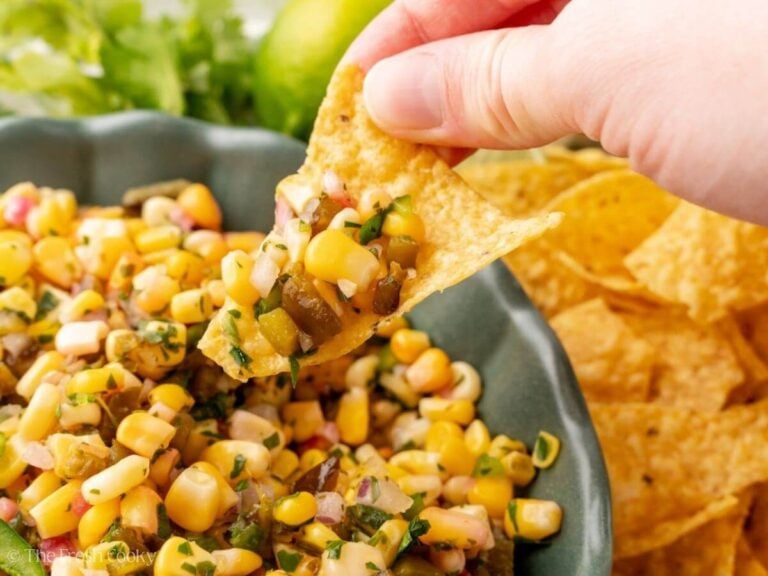 Hand dipping a tortilla chip into a bowl of chipotle corn salsa.
